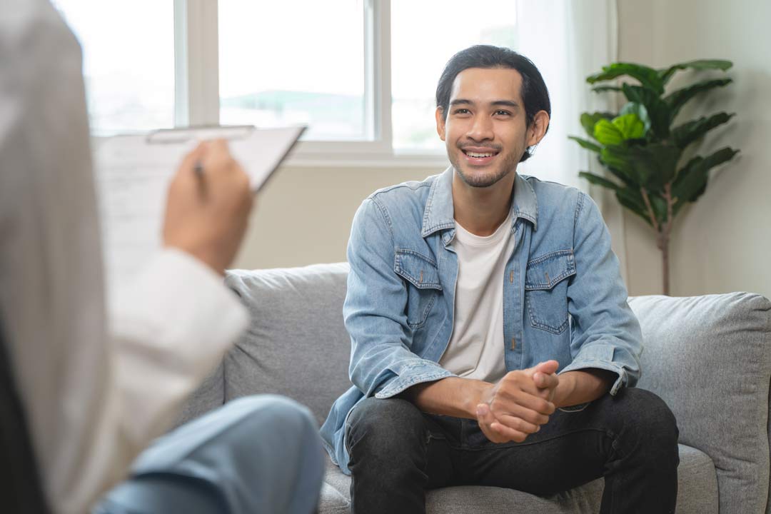 Person with a clipboard speaking with another person sitting on a couch